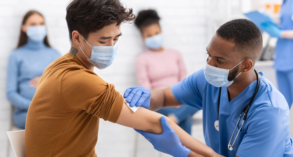 Asian Man Receiving Coronavirus Vaccine Intramuscular Injection In Arm During Doctor's Appointment In Hospital